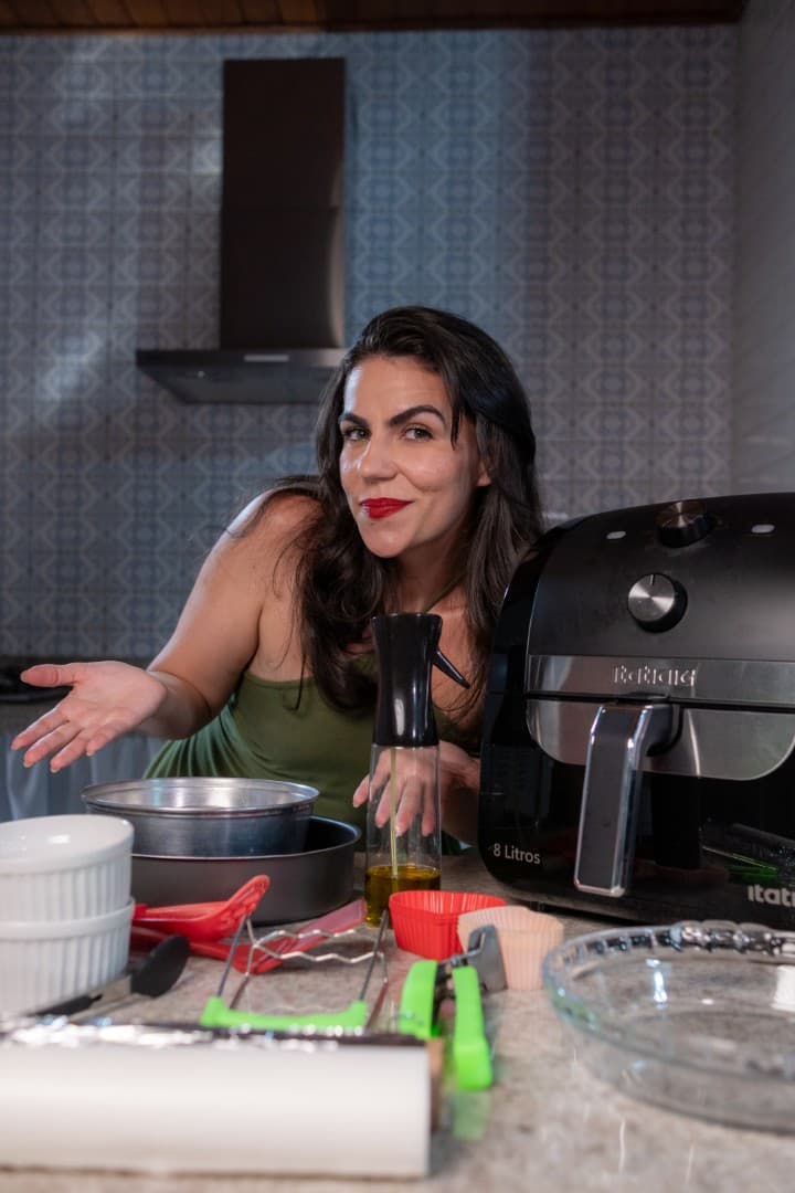 Cecília na cozinha com uma air fryer preta.