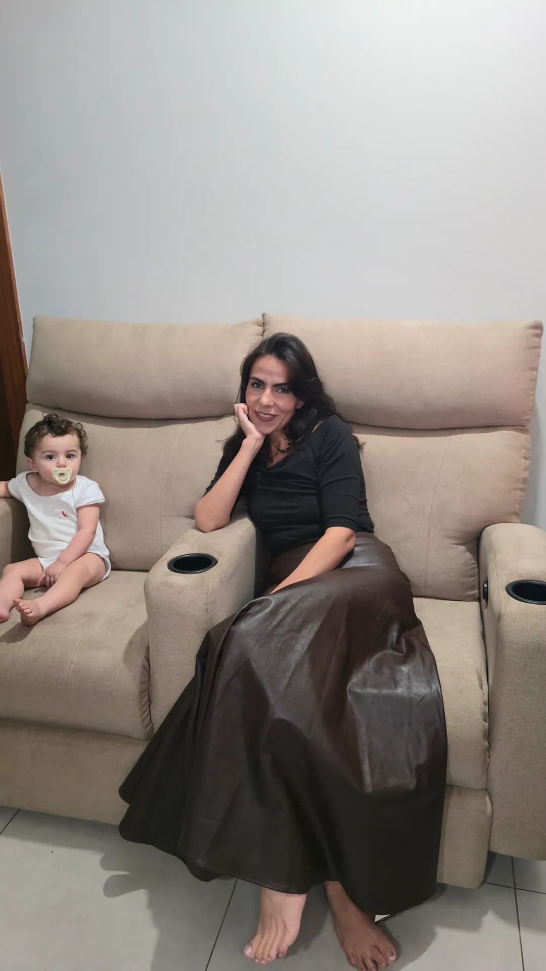 Cecília e o Ian sentados na poltrona reclinável bege da sala de estar.