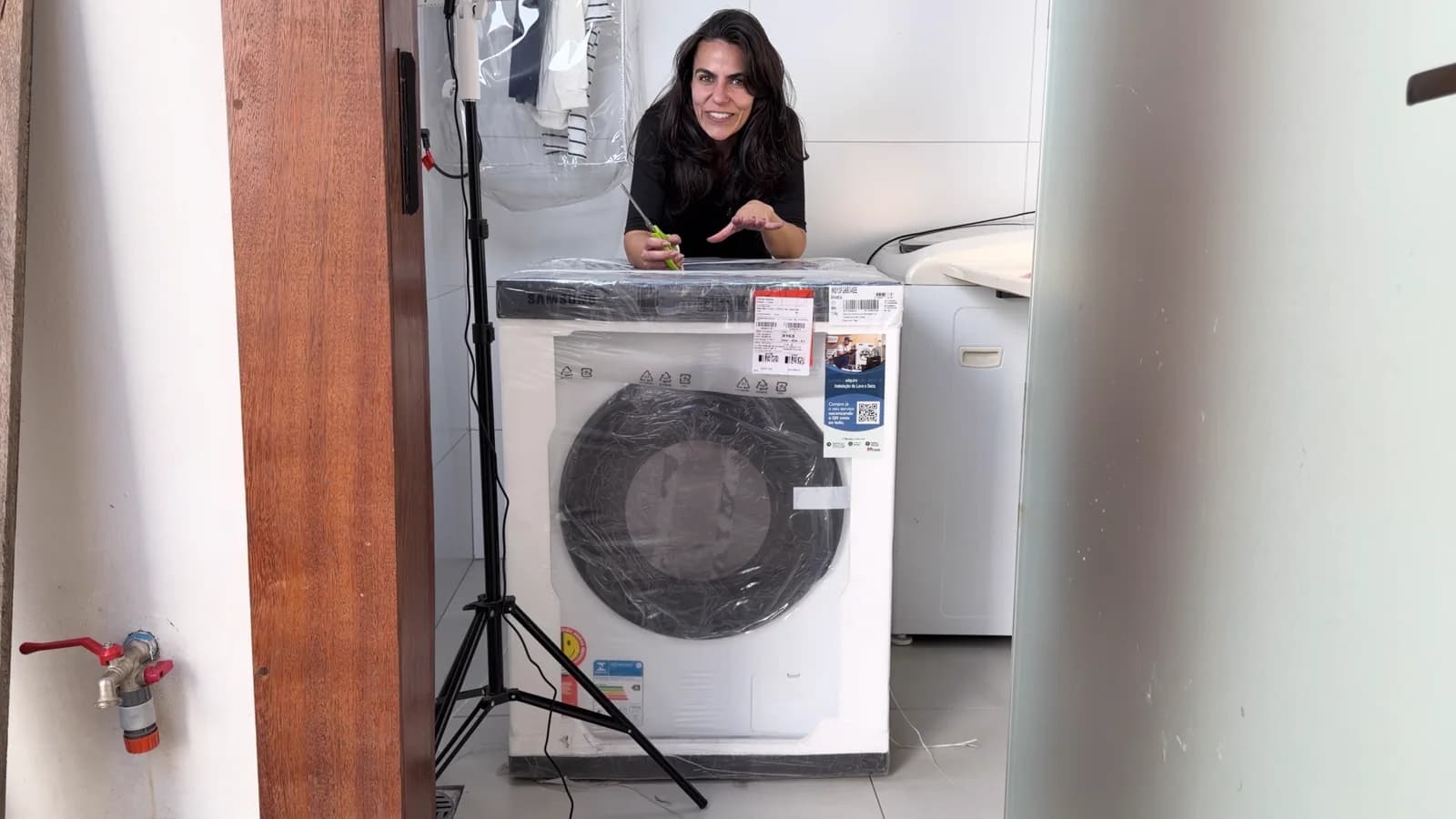 Cecília atrás da lava e seca Samsung ainda no plástico na lavanderia