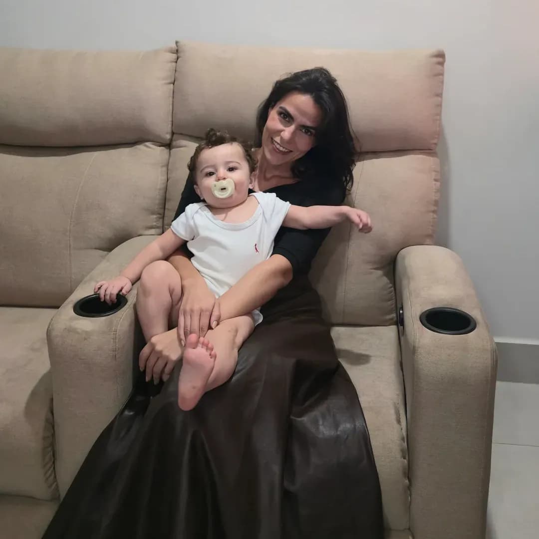 Cecília sentada com o Ian no colo na poltrona reclinável bege da sala