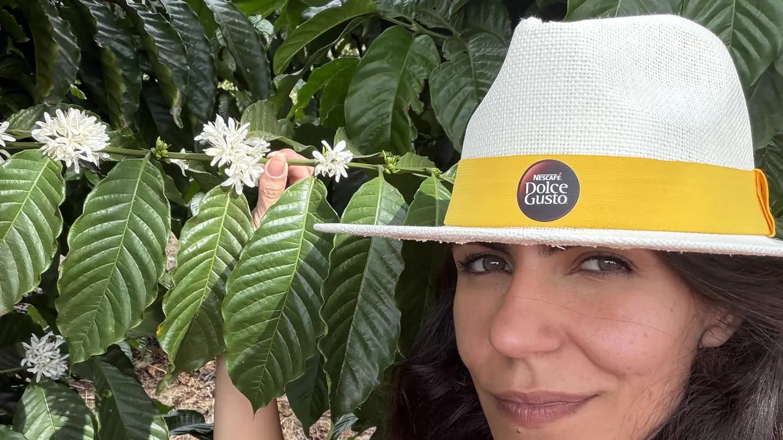 Cecília Mauad, com chapéu da NESCAFÉ Dolce Gusto, entre pés de café em flor