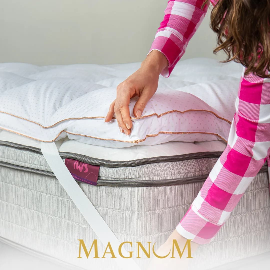 Foto oficial da I Wanna Sleep: mulher afofando o Pillow Top Magnum sobre o colchão, com o elástico lateral à mostra