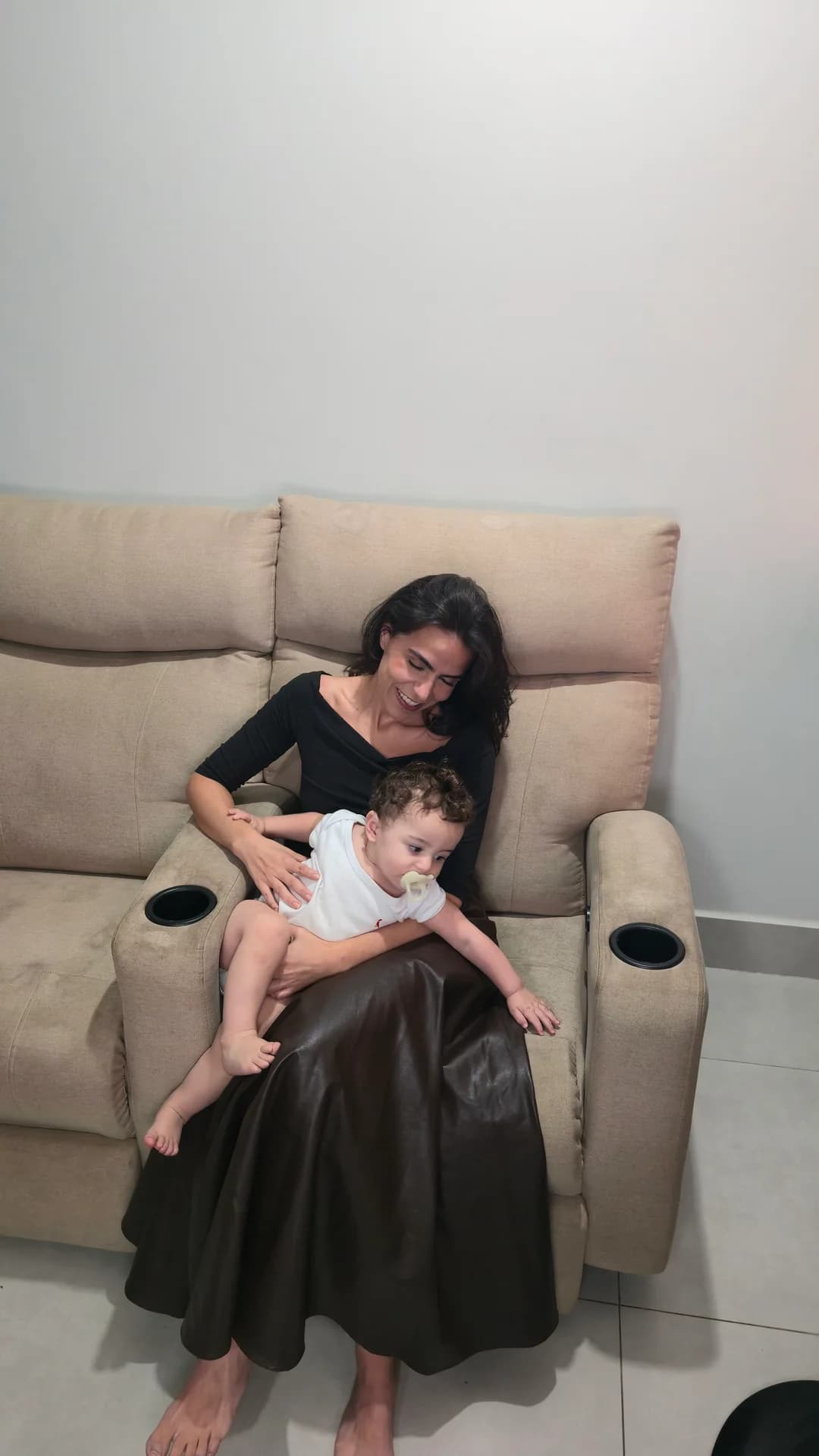 Cecília com o Ian no colo na poltrona reclinável bege.