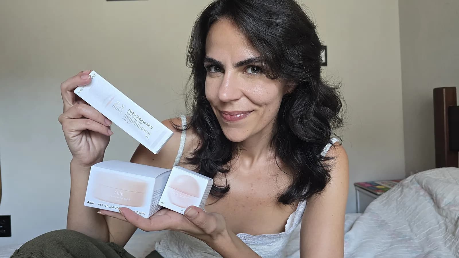 Cecília Mauad segurando as caixas do creme booster PDRN, do adesivo de hidrogel para os olhos e da máscara labial da Abib