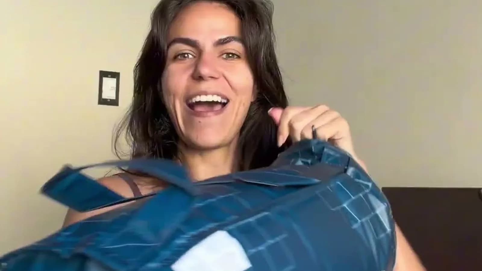 Cecília Mauad, do Em Casa com Cecília, sorrindo com a embalagem do cobertor Igloo da I Wanna Sleep no quarto